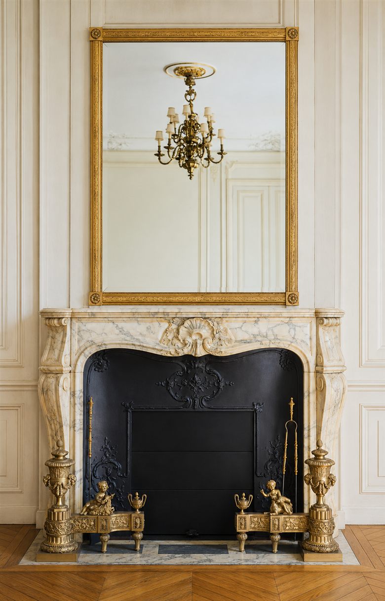 Cheminée en marbre blanc avec miroir doré, chandelier en bronze et chenets sculptés — élément central du salon classique parisien