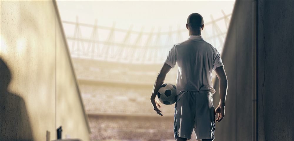 Footballeur professionnel sortant du tunnel d'un stade au coucher du soleil, ballon à la main
